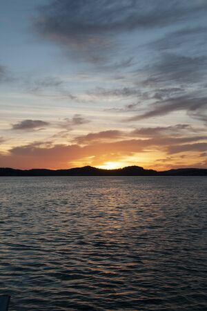 A delicate orange and grey coloured stratocumulus cloudy coastal sunrise seascape in a blue sky over the sea with water reflections. Gosford, New South Wales, Australia.の写真素材