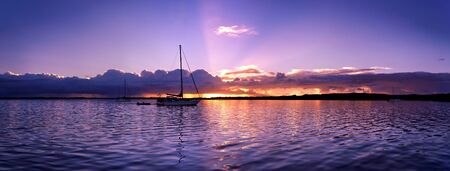 An tranquil pastel mauve coloured nautical waterscape sunset panorama in a blue sky reflected in smooth tropical ocean waters. Tin Can Bay, Queensland, Australia.の写真素材