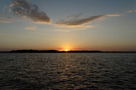A natural tranquill orange coloured cumulus cloudy ocean sunset seascape over sea water with water reflections.の写真素材