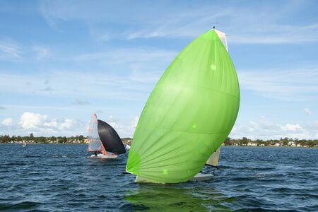 Kids sailing small sailboat head-on closeup with a fully deployed lime green spinnaker being closley followed by a competitor with a black coloured sail. Junior sailors racing on saltwater Lake Macquarie. Photo for commercial use.の写真素材