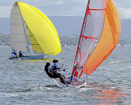 Children Sailing small sailboats with yellow and orange sails in competition. Teamwork by junior sailors racing on saltwater Lake Macquarie. Photo for commercial use.の写真素材