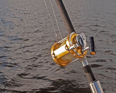 a gold coloured Big Game 50 wide fishing reel closeup in used condition. Located in a rod holder aboard a yacht, ready to deploy.の写真素材