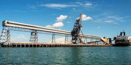 Port of Gladstone. Waterfront maritime commercial coal loading marina/dock panorama with a moored ship in tropical water with cumulus cloud in blue sky. Gladstone Harbour, Queensland, Australia.の写真素材