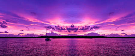 A bright  pink magenta coloured cloudy nautical coastal sunrise seascape in a purple sky over the ocean with sea water reflections. Nature background image. Queensland, Australia.の写真素材