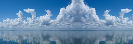 Nephology at its best. A beautiful meteorological sky cloudscape scene, with white  Cumulonimbus cloud formation in a mid blue sky with ocean water reflections. Atmospheric beauty in nature. New South Wales, Australia.の写真素材