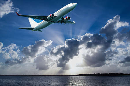 Jet aircraft departing Mascot Airport flyng over Botany Bay in a vibrant blue sky, with bright white coloured Sun Rays and cumulonimbus clouds. Sydney, New South Wales, Australia.の写真素材