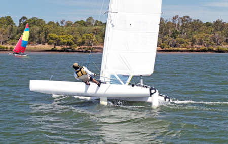 Youth Sailing small catamaran boat with a white sail on an inland waterway. Sailing for fun and in competition. Bundaberg, Australia. Photo for commercial use.の写真素材