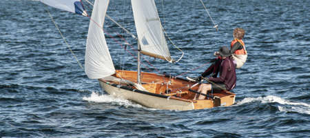 Children sailing small dinghy with white sails up-close on an inland waterway. Teamwork by junior sailors racing on saltwater Lake Macquarie. Photo for commercial use.の写真素材