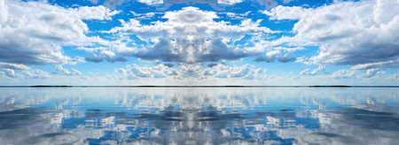 A beautiful meteorological sky cloudscape panorama, with white Cumulus cloud formation in a bright blue sky over smooth ocean water with clear water reflection. New South Wales, Australia.の写真素材