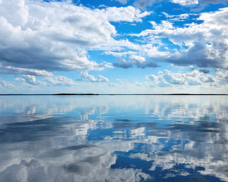 Nephology at its best. A beautiful meteorological sky cloudscape scene, with white Cumulus cloud formation in a mid blue sky over ocean water with reflections. Seascape beauty in nature. New South Wales, Australia.の写真素材