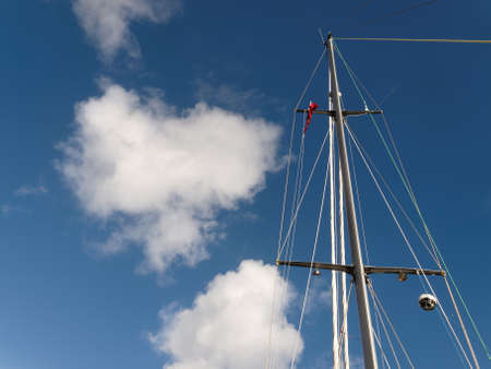 A sunny day nautical nature scene. A yacht mast with rigging high in a bright blue sky with white fluffy Cumulus clouds. New South Wales, Australia.の写真素材
