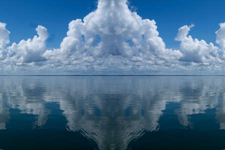 Nephology at its best. A beautiful meteorological sky cloudscape scene, with white Cumulonimbus cloud formation in a mid blue sky with clear ocean water reflections. Atmospheric beauty in nature. New South Wales, Australia.の写真素材