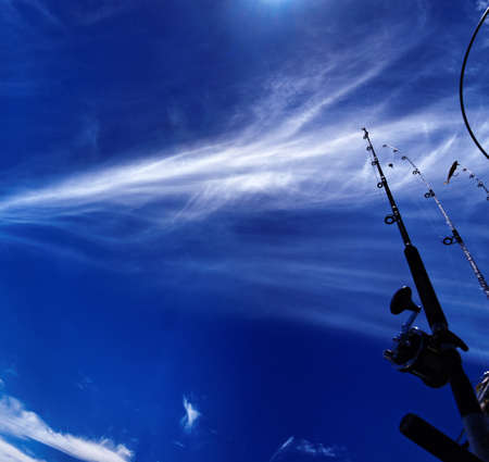 Atmospheric photography. A beautiful meteorological cloudscape scene, with white  cloud formation in a mid blue sky with fishing rods in the foreground. Nephology art.の写真素材