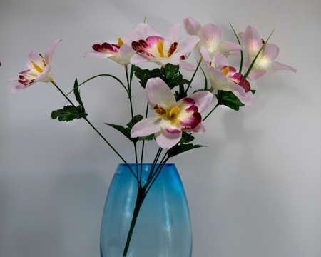 Artificial flower display in a blue glass vase isolated on a white background. Closeup photo.の写真素材