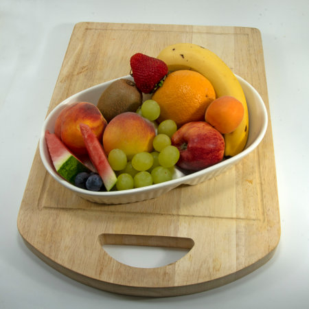Colourful tropical fresh fruit collection in a bowl on a wood cutting board closeup including mango strawberry & banana isolated on white. High view natural fruit image.の写真素材