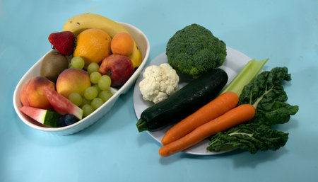 Food selection. Colourful collection of fresh fruit and vegetables including mango grapes kiwi fruit carrots spinach and broccoli, isolated on a light blue background.の写真素材