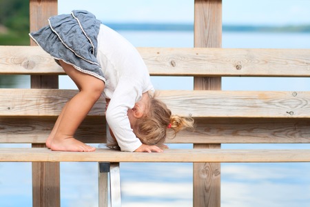 Funny little girl standing head over heels on the pier outdoorsの写真素材