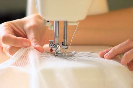 The process of sewing curtains from a mesh of white fabric. The rolled edge of the fabric is placed...