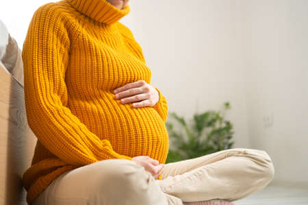A cute pregnant woman sits and holds her hand on her belly. The concept of a happy pregnancy in anticipation of a baby. 9 months of waiting for a baby.の写真素材