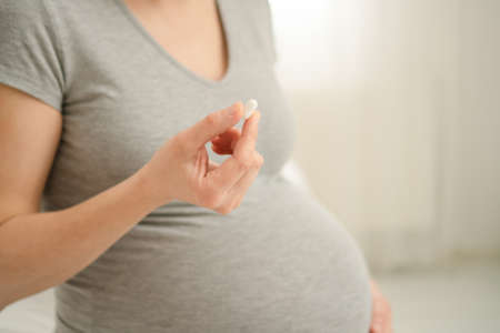 Close-up view of pill in hand. In the background is a pregnant woman. Taking vitamins during pregnancy. Health care and medication during pregnancy and childbearing.の写真素材
