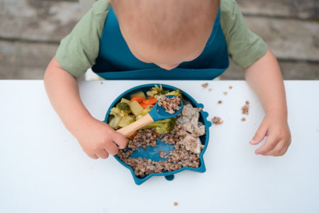 Overhead shot of a toddler eating their first meal outdoors with a spoon. Healthy and delicious vegetables.の写真素材