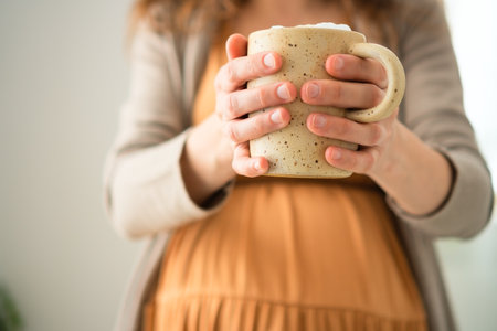 Pregnant female holding warm coffee while relaxing at home. Modern approach to moderate caffeine consumption during pregnancy.の写真素材