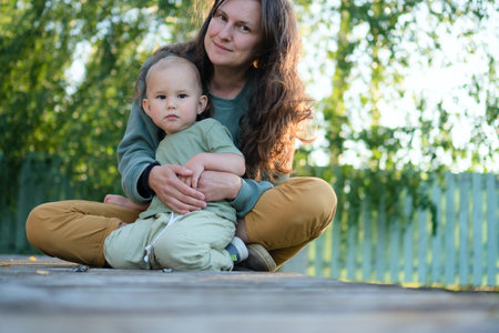 Content mother cuddles her smiling toddler amidst beautiful natural surroundings. Authentic moment of parental love and childhood wonder in the outdoors.の写真素材
