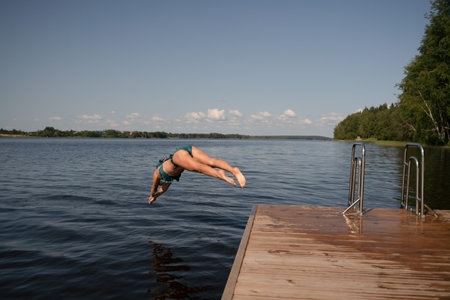 Fit woman diving headfirst from pier into lake. Healthy body, strong motion, natural summer activity.の写真素材