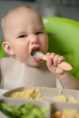 Happy baby exploring nutritious meal with hands - corn porridge, steamed broccoli and boiled egg pieces. Natural weaning process and food discovery moment.の写真素材
