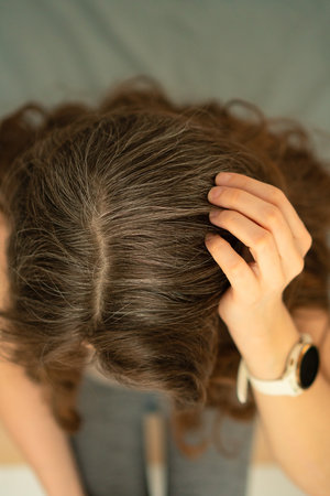 Close-up top view of mature woman grasping her head, showing natural gray hair. Concept of aging,...