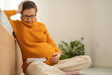 Serene pregnant female writing important delivery reminders in notebook at home. Thoughtful preparation for maternity ward and newborn care essentials.の写真素材