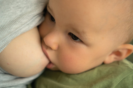 Close-up of happy contented toddler nursing at mothers breast. Natural moment of bonding and...