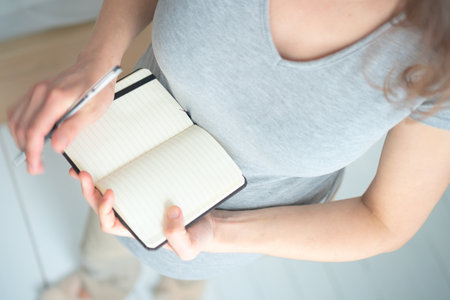 Overhead shot of future mother writing crucial to-do list for maternity period. Detailed organization of hospital bag and birth preparation notes.の写真素材