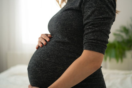 Detailed shot of pregnant womans hands softly stroking her rounded abdomen. Intimate moment of...