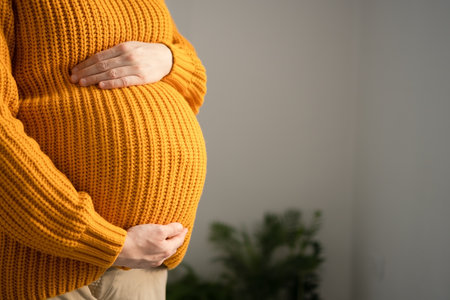 Serene close-up of pregnant womans hands lovingly touching her baby bump. Heartwarming scene of prenatal connection in cozy home environment.の写真素材