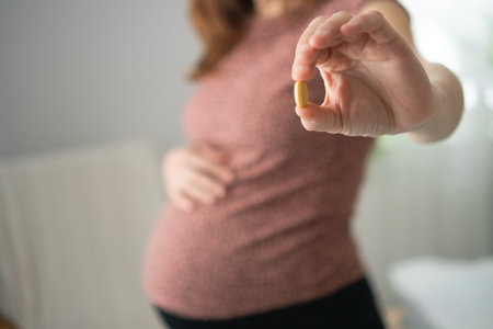 Pregnant female carefully examining pill before intake while touching her bump. Thoughtful health...