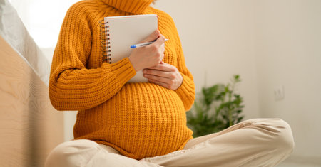 Close view of pregnant woman carefully compiling birth essentials list. Organized notes for maternity bag and important delivery reminders.の写真素材