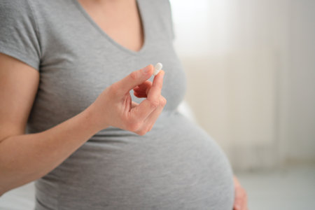 Close-up shot of expecting mothers hand holding prescribed tablet while other hand protects her belly. Cautious healthcare during pregnancy.の写真素材