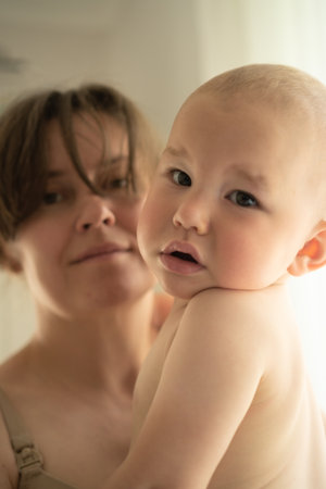 Serene home scene of mother cradling her little one with unconditional love. Beautiful natural moment of maternal affection and quiet connection.の写真素材