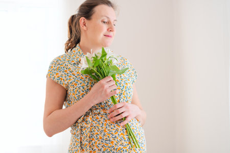 Delicate white blossoms complement expecting mothers gentle belly caress. Intimate moment of pregnancy joy and natural beauty.の写真素材