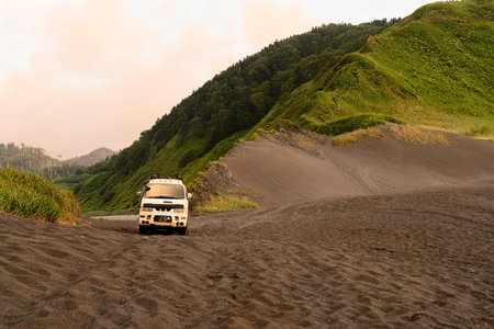 Durable expedition vehicle standing alone at untouched beach with dramatic mountain ridges meeting ocean. Ideal for adventure tourism and van life content.の写真素材