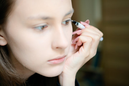 A beautiful teenage girl drawing winged eyeliner on her eyes in a close-up shot. Self-applied makeup highlights her youthful style and confident, polished appearance.の写真素材