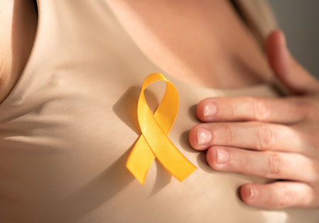 Detailed shot of yellow satin ribbon attached to females shirt, representing hope and solidarity with children battling cancer.の写真素材