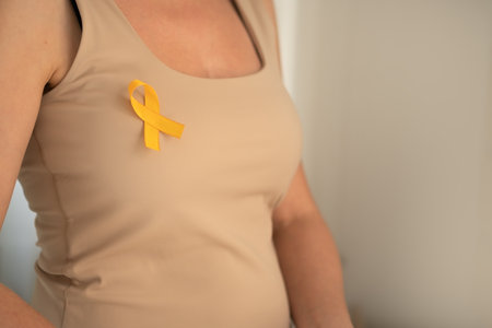 Close-up shot of yellow ribbon fastened to females top, symbolizing support and awareness for kids fighting cancer and their families.の写真素材