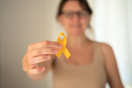 Womans hand carefully holding yellow awareness ribbon, representing compassion and support for children fighting cancer and their families.の写真素材