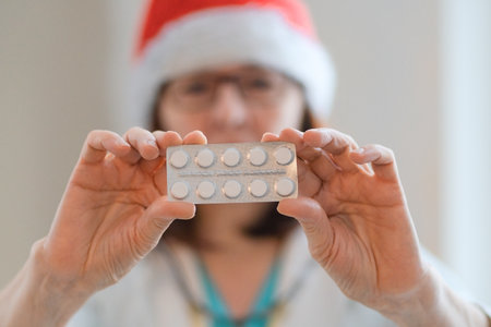 Portrait of female doctor in medical coat and Santa hat. Holding tablets forward. Focus on health, treatment, and care during holiday flu season. Medicine support in festive winter time.の写真素材