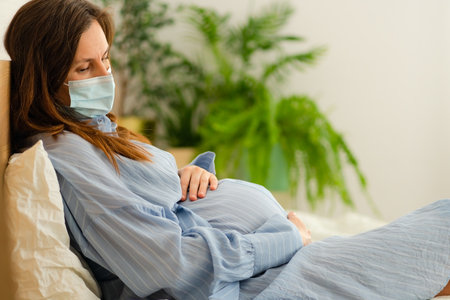 Future mother wearing protective mask while resting in bed. Managing illness symptoms responsibly during pregnancy.の写真素材