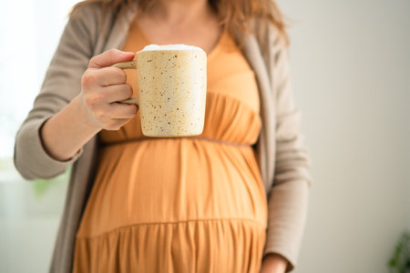 Expecting mother carefully sipping coffee at home. Balanced approach to caffeine consumption during pregnancy with doctors approval.の写真素材