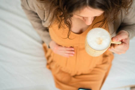 Mom-to-be savoring warm coffee drink in peaceful home setting. Responsible caffeine intake discussion during gestation period.の写真素材