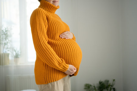 Serene close-up of pregnant womans hands lovingly touching her baby bump. Heartwarming scene of prenatal connection in cozy home environment.の写真素材